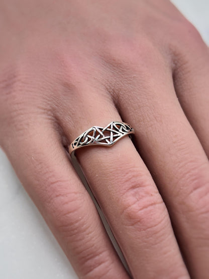 May include: A silver-colored ring with a Celtic knot design. The ring features an intricate pattern of interwoven lines forming a decorative band. The ring is worn on a finger, showcasing the detailed craftsmanship and the ring's elegant style.