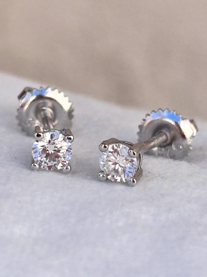 May include: A pair of sparkling diamond stud earrings. Each earring features a round, brilliant-cut diamond set in a four-prong setting. The posts have a screw-back closure. The earrings are set against a soft, neutral background.